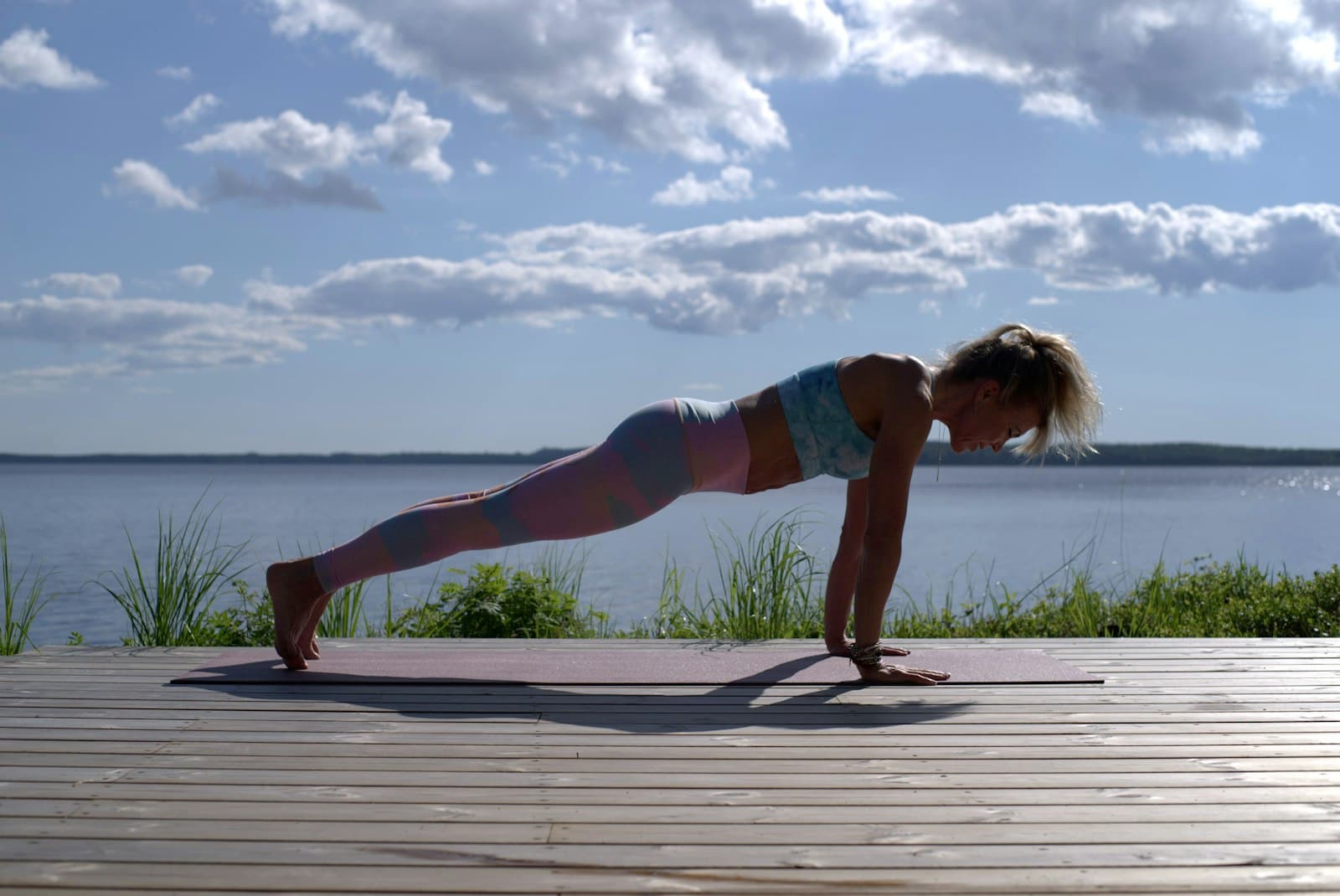 Frau hält eine Plank-Position auf einem Steg am See
