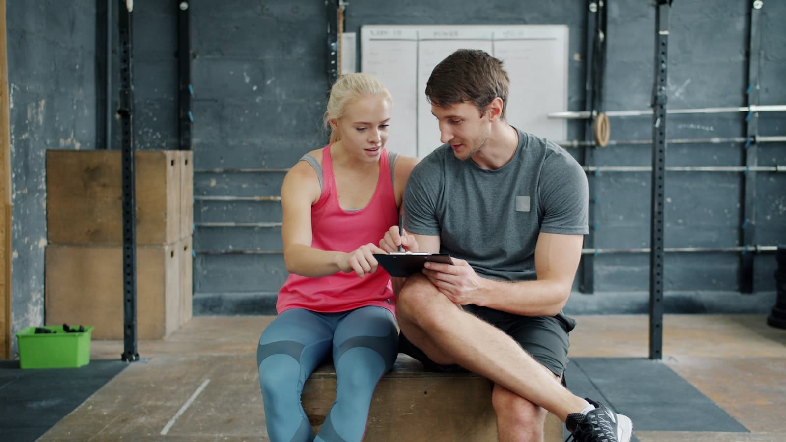Trainer und Kundin besprechen einen Trainingsplan auf einem Tablet im Fitnesscenter